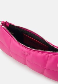 Felroze leren pouch met zilveren rits, gekruist ontwerpen en in het leer geperst "HUGO" logo aan de voorkant, gedeeltelijk open met zwarte binnenvoering zichtbaar.