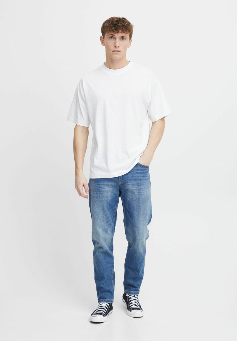 Camiseta blanca de algodón con mangas cortas, combinada con jeans de denim azul y zapatillas negras. La tela parece suave y casual.