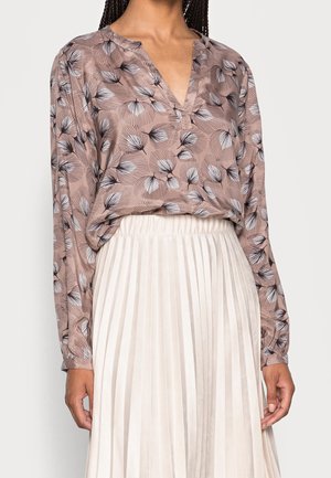 Lange mouw mauve blouse met zwart-wit bloemenpatroon, ingestopt in een hooggesneden witte geplooide rok.