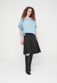 Φαρδιά γαλάζια φούτερ με μπροστινή τσέπη και λευκά κορδόνια, σε συνδυασμό με πλισέ μαύρη τζιν φούστα και μαύρες μπότες μέχρι το γόνατο.