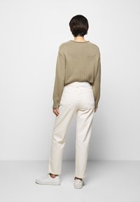 Brązowy sweter teksturowany w połączeniu z białymi spodniami o wysokim stanem i białymi sneakersami, pokazany z tyłu na neutralnym tle.