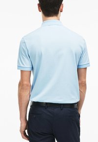 Ljusblå pikétröja med korta ärmar, krage och textilstrukturer. Buren med mörkblå byxor och ett svart bälte.