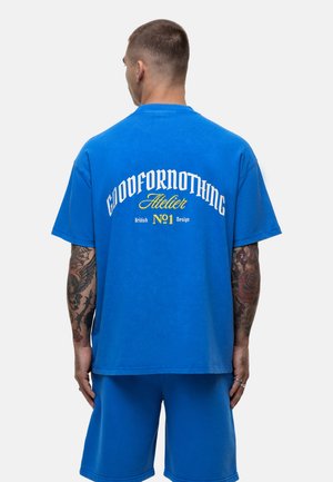 Blauses Baumwoll-T-Shirt mit kurzen Ärmeln, das auf der Rückseite mit einem großen weißen und gelben Logo-Text versehen ist. Kombiniert mit passenden blauen Shorts.