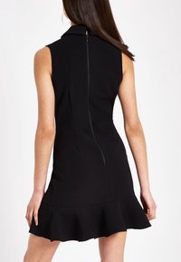 Svart ärmlös klänning med krage, figursydd överdel och en utsvängd volangkant. Har en dold dragkedja i ryggen och en slät tygtextur.