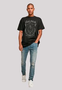 Black graphic t-shirt featuring "Black Sabbath" print, paired with light blue distressed jeans and white sneakers. Casual fit with short sleeves.