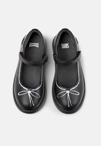 Czarne skórzane buty typu Mary Jane z białym wzorem kokardy. Posiadają rzep oraz okrągły czubek. Wnętrze zawiera logotypy Camper oraz Twins.