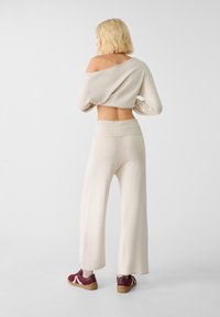 Maglione cropped beige con design off-shoulder e maniche larghe abbinato a pantaloni a gamba larga alta vita in un morbido tessuto a maglia.