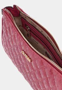 Rød quiltet taske med guldlås og logo. Indvendigt med lynlåslomme og mønstret foring. Glat tekstur med struktureret form.