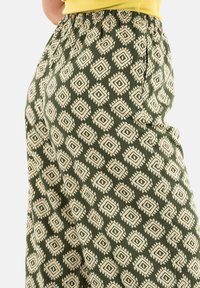 Pantaloni verdi con motivo a fantasia, dalla consistenza morbida, caratterizzati da forme a diamante color crema e accenti appuntiti, dotati di vita elastica e vestibilità ampia.