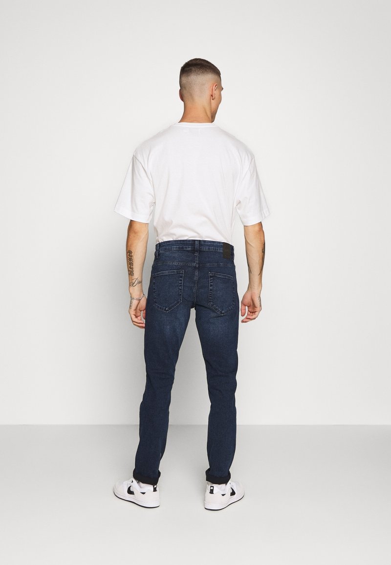 Mörkblå denimjeans med smal passform, med bakfickor och en midjeband, tillsammans med en vit t-shirt med kort ärm och sneakers.