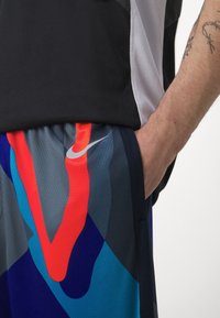 Spodenki sportowe Nike wykonane z siateczkowej tkaniny w ciemnym niebieskim kolorze, ozdobione żywymi, abstrakcyjnymi wzorami w kolorach czerwonym, jasnoniebieskim i szarym oraz białym logo po boku.
