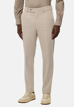 Pantalones beige con una textura suave, con cierre de botón, bolsillos laterales y un corte ajustado, combinados con zapatillas de color claro.