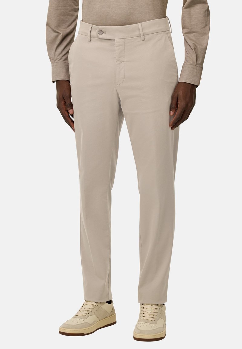 Pantalons beige avec une texture lisse, dotés d'une fermeture à bouton, de poches latérales et d'une coupe ajustée, associés à des baskets de couleur claire.