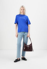 Blauwe T-shirt met korte mouwen met de opdruk "FEMME", gecombineerd met lichtblauwe jeans en een bordeauxleren schoudertas met een zilveren gesp.