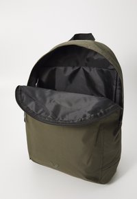 Mochila de tela verde con cierre de cremallera y forro interior negro. Presenta una parte superior redondeada y un logotipo sutil cerca de la base.