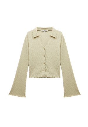 Lichtbeige cropped overhemd met knopen, lange klokmouwen en een textuurstof. Heeft een kraag en vijf knopen aan de voorkant.