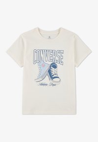 Kremfarget t-skjorte med et grafisk motiv av to joggesko i blått og hvitt; fet "CONVERSE" tekst over og "Athletic Dept." under i blått.