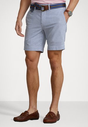 Pantaloni corti a righe blu e bianche con una cintura a strisce orizzontali. Il materiale è leggero. Il design include tasche laterali e una vestibilità sagomata.