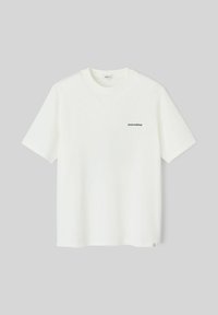 T-shirt en coton blanc à manches courtes, avec un texte "Untroubled" en vert sur la poitrine et une petite étiquette verte au bas.