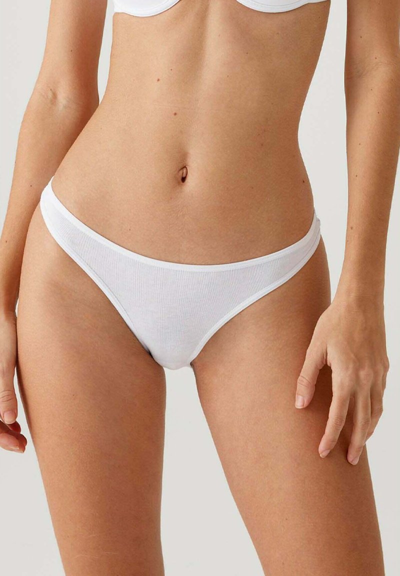 Witte katoenen stringonderbroek met een zachte ribbeltextuur, lage taille en minimale bedekking. Voorzien van een dunne elastische tailleband.