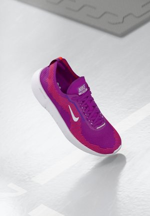Chaussure de running Nike violette et rose avec logo Swoosh blanc et semelle blanche, montrée flottant au-dessus d'un sol gris clair avec des marquages.