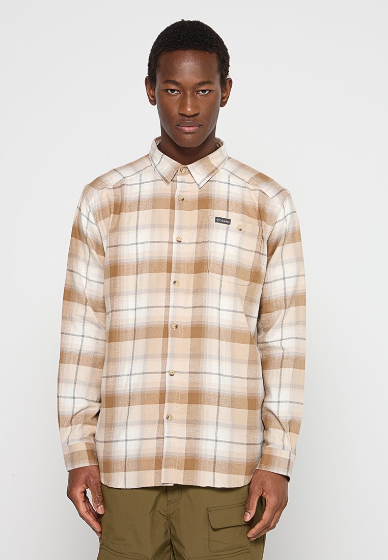 Camisa de franela de cuadros marrones y beige con cuello abotonado, bolsillo en el pecho y etiqueta de marca. Presenta botones en la parte delantera y mangas largas.