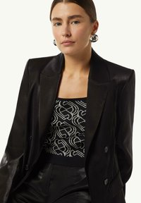 Black double-breasted blazer with a sleek finish, paired with a fitted patterned top featuring white geometric designs on a black background.