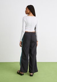 White ribbed cropped long-sleeve top with scalloped hem paired with black wide-leg pants featuring teal side stripes and elastic waistband.