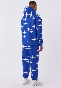 Sudadera con capucha y pantalones a juego en color azul con un patrón de estrellas blancas, fabricados con un tejido suave. El ajuste es relajado con puños de canalé y capucha.