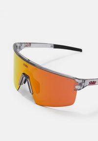 Gafas de sol con montura transparente, lentes de degradado naranja, forma de escudo grande y patillas texturizadas negras. Logo impreso en la montura.