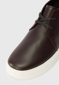 Pruun nahast spordijalanõud vaadatuna ülevalt, millel on ümar varvas, hallad paelad ja valge kummitald tekstuuriga detailiga.