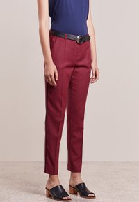Pantalon à carreaux rouge avec une coupe ajustée, poches latérales fendues et ceinture en cuir noir avec une boucle ronde, associé à des mules noires.