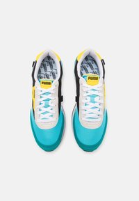 Blauwe en zwarte sneakers met een gestructureerde afwerking, featuring witte veters en een gele accent. Het interieur toont een herhalend patroon.