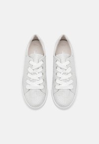 Baskets blanches avec une texture tissée, dotées de lacets blancs plats, de semelles en caoutchouc et d'un design minimaliste sans marquage apparent.