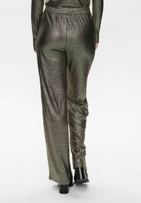 Pantaloni metalici de culoare verde măsline, cu un finisaj texturat, design cu picioare largi, talie elastică și asortați cu pantofi cu toc negri.