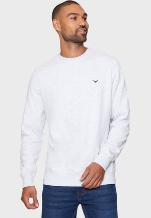 Sudadera de cuello redondo gris claro en material suave, con un pequeño logo azul marino en el pecho, combinada con jeans azules.