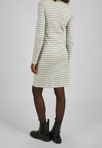 Robe en maille à rayures verticales grises et blanches, manches longues, longueur au genou, portée avec des bottines noires.