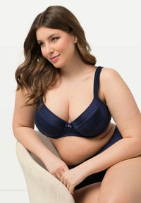 Navy blue rintaliivi ja alushousut, joissa on uritettu pinta, pitsiyksityiskohtia ja nauhakiinnitys etuosassa. Säädettävät olkaimet, täydellinen peittävyys.