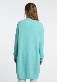 Tyrkis stickad kofta, lång design, lös passform, ribbade muddarna och nederkant, mjuk textur, inga synliga knäppningar eller mönster.