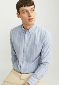 Šviesiai mėlyna marškiniai su apykakle, vertikaliomis baltomis ir rožinėmis juostelėmis, mygtukų užsegimas, ir viena kišenė kairėje pusėje. Lygus audinio paviršius.