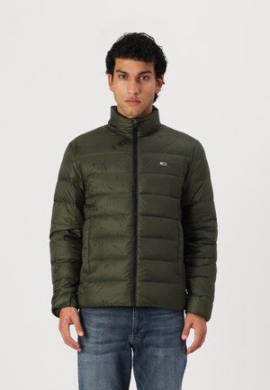 Giacca puffer verde oliva con colletto alto, chiusura frontale con zip, due tasche laterali, texture trapuntata e un piccolo logo sul lato sinistro del petto.