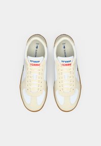 Chaussures de tennis blanches et beiges avec une semelle en gomme, dotées d'un design à lacets, d'une tige en textile souple et d'un motif "TENNIS" sur la languette.