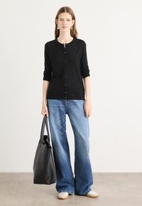 Svart langermet cardigan med knappelukking, kombinert med lyseblå vide jeans og en svart tote-bag. Hvite joggesko fullfører antrekket.