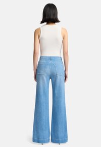 Helle blaue, hochgeschnittene, ausgestellt geschnittene Jeans mit weitem Bein, ausgestattet mit Gesäßtaschen und einem sauberen Saum. Getragen mit einem weißen Tanktop.