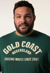 Zelené tričko s kulatým výstřihem, s potiskem "GOLD COAST" a "CHASING WAVES SINCE 2007" v krémové barvě. Měkká textilie.