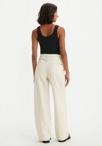 Wijd-uitlopende crèmekleurige broek van denim, met een hoge taille, twee achterzakken en een subtiele merketiket. Soepele textuur en een relaxte pasvorm.