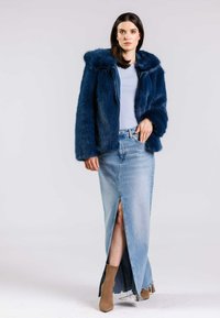 Marinblå fake fur-jacka med huva, ljusblå topp och jeanskjol med hög slits. Modellen bär tan-färgade ankelsockor och spetsiga klackskor.