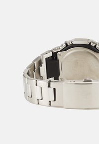 Montre en acier inoxydable argenté avec un boîtier en résine noire, dotée d'un bracelet segmenté et d'un mécanisme de fermoir, montrant les détails du fond de la montre.