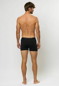Boxeri negri din material elastic, cu un design ajustat și talie elastică, având un logo. Materialul pare neted și flexibil.