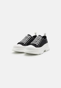 Schwarze Leinensneaker mit weißen Gummisohlen, runden Schnürsenkeln, einer Zuglasche und kontrastierenden Nähten. Dicke, strukturierte Sohle.